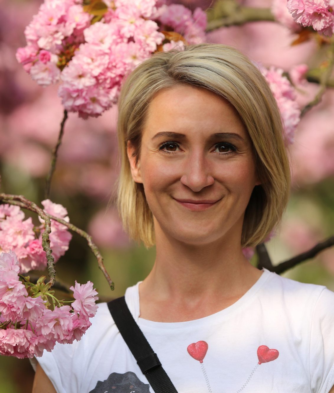 Tiersitterin in Potsdam Tiersitterin lächelt auf Profilbild vor blühenden Kirschbäumen, trägt ein T-Shirt mit Herzmotiv.